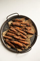 unwashed carrots in a metal tray on a white background