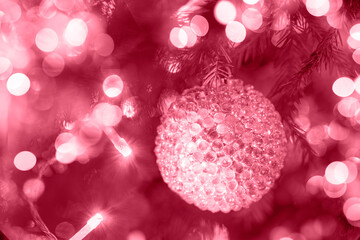 Glass textured Christmas ball hanging in Xmas tree with holiday lights in color 2023 Viva Magenta.