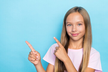 Portrait of good mood small girl straight hairstyle wear pink t-shirt fingers indicating empty space isolated on blue color background