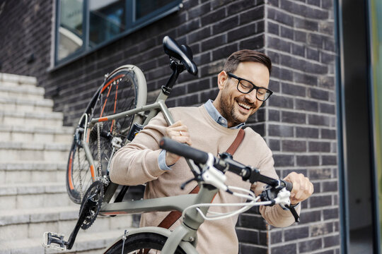A casual businessman is carrying his bicycle on shoulder.