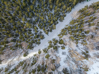 Flight over the winter mountains with road serpentine and pine forest. Top down view. Landscape photography