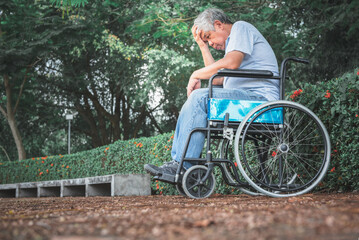 Asian elderly man sitting in a wheelchair in the park. He has symptoms of depression and stress...