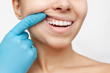 Cropped shot of a young woman's face with doctor's hand in a blue glove showing healthy gums...