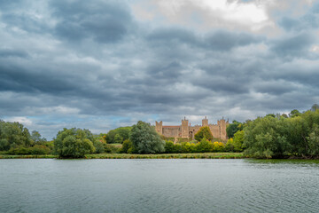Fototapeta na wymiar Distant view of a English castle seen across a large lake. Menacing skies appear before the start of a storm.