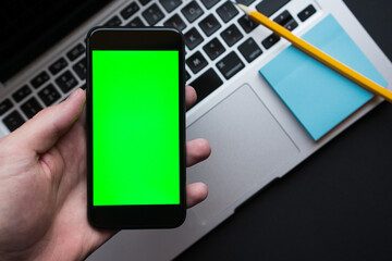 Man holding smartphone with green chroma key screen, on background modern black office desk table...