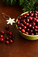 green bowl of cranberries with snowflake ornament on wood table