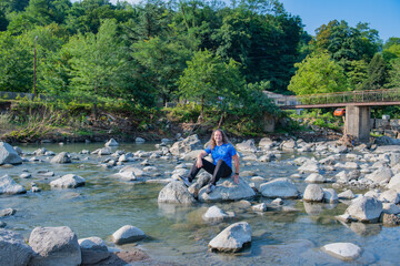 In blue clothes, a man sits on a stone by the river