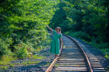 a woman in a green dress walks along the railway