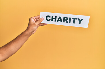 Hand of caucasian man holding paper with charity word over isolated yellow background