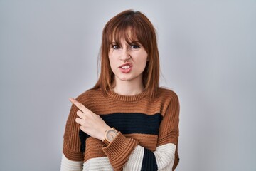 Young beautiful woman wearing striped sweater over isolated background pointing aside worried and...
