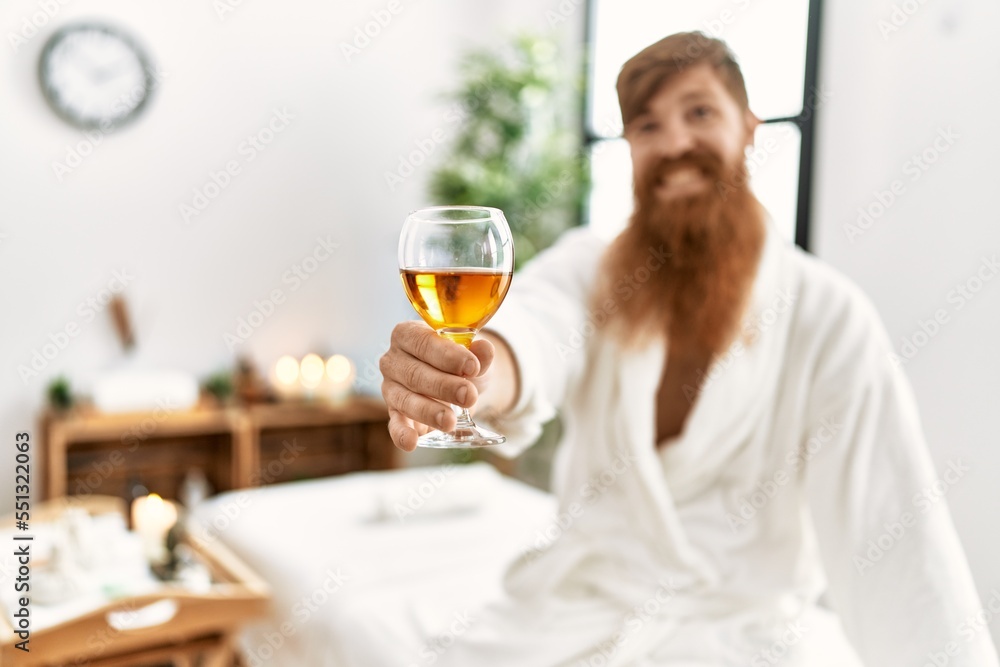 Sticker Young redhead man wearing bathrobe drinking champagne at beauty center