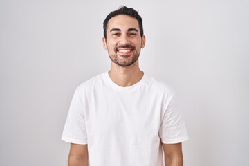 Handsome hispanic man standing over white background with a happy and cool smile on face. lucky...