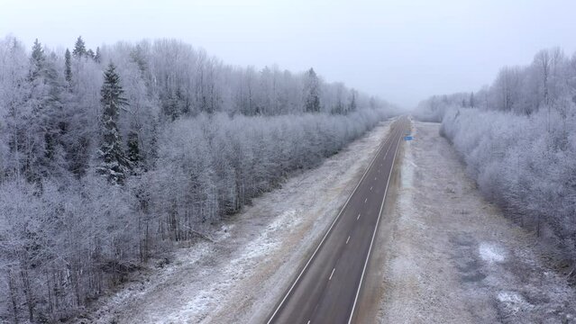 Winter road with a forest in the fog. Road and trees covered with snow and frost in early winter