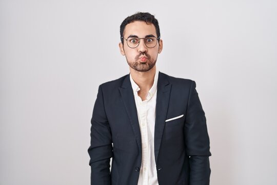 Handsome business hispanic man standing over white background puffing cheeks with funny face. mouth inflated with air, crazy expression.