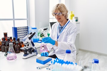 Fototapeta premium Young blond man scientist smiling confident weighing test tube at laboratory