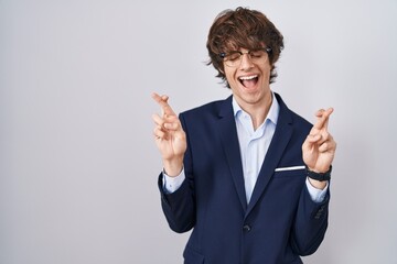 Hispanic business young man wearing glasses gesturing finger crossed smiling with hope and eyes closed. luck and superstitious concept.