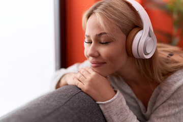 Young blonde woman listening to music sitting on sofa at home