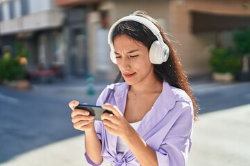 Young beautiful hispanic woman playing video game with serious expression at street