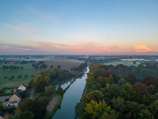 Panorama of dramatic and colorful sky over Fields, trees and River or canal from a drone during sunset or sunrise. High quality photo