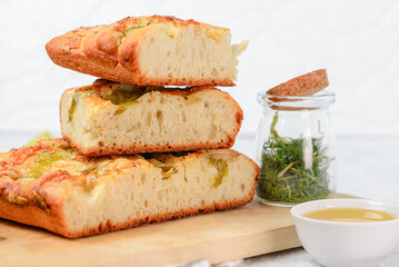 Stack of  bread slices of focaccia on wooden stand with dried herbs in a jar and olive oil in a bowl