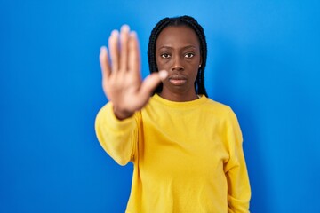 Beautiful black woman standing over blue background doing stop sing with palm of the hand. warning expression with negative and serious gesture on the face.