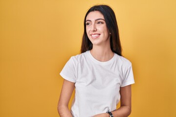 Obraz premium Young beautiful woman standing over yellow background looking away to side with smile on face, natural expression. laughing confident.