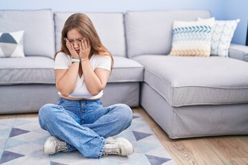 Obraz premium Young caucasian woman sitting on the floor at the living room with sad expression covering face with hands while crying. depression concept.