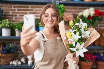 Young blonde woman florist taking selfie with flowers bouquet at florist