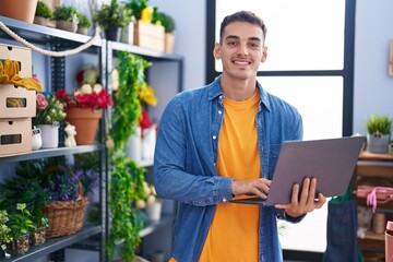 Young hispanic man florist smiling confident using laptop at florist store
