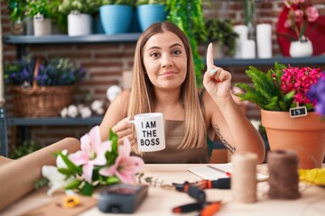 Young blonde woman working at florist shop holding i am the boss cup smiling with an idea or question pointing finger with happy face, number one