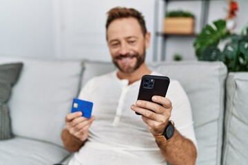 Middle age hispanic man using smartphone and credit card at home
