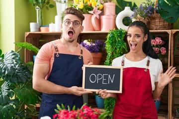 Young hispanic man a woman working at florist holding open sign celebrating crazy and amazed for success with open eyes screaming excited.