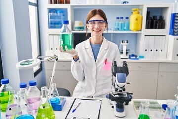 Young brunette woman working at scientist laboratory looking positive and happy standing and smiling with a confident smile showing teeth