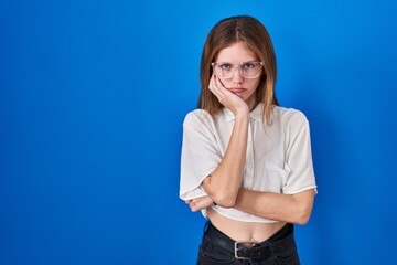 Beautiful woman standing over blue background thinking looking tired and bored with depression problems with crossed arms.