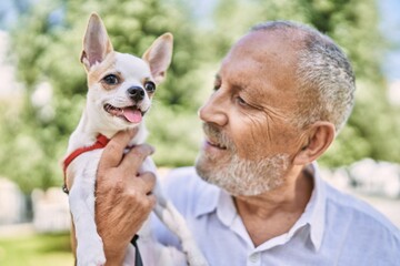 Senior man smiling confident hugging chihuahua at park