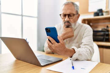Senior grey-haired man using smartphone working at office
