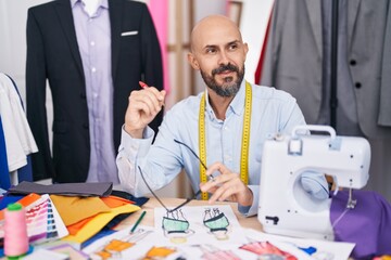 Young bald man tailor smiling confident holding glasses at tailor shop