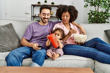 Couple and daughter watching movie sitting on sofa at home