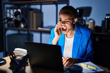 Beautiful african american woman working at the office at night shouting and screaming loud to side with hand on mouth. communication concept.