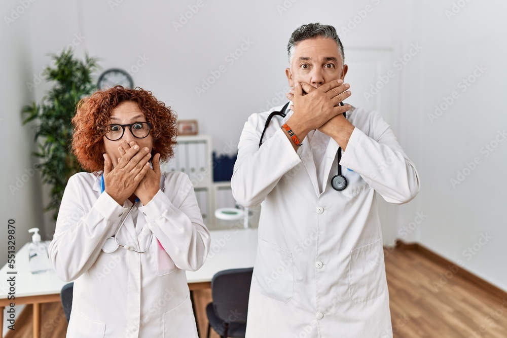 Poster Two middle age doctors at medical clinic shocked covering mouth with hands for mistake. secret concept.