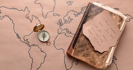 Old book, compass and paper sheet on world map. Travel concept