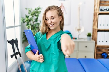 Young caucasian woman working at pain recovery clinic pointing to you and the camera with fingers, smiling positive and cheerful