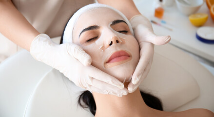 Cosmetologist applying mask onto woman's face in beauty salon