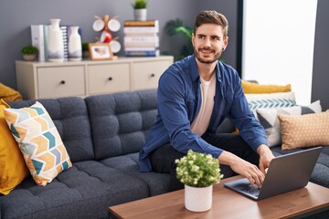 Young caucasian man using laptop sitting on sofa at home