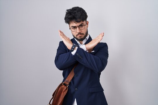 Hispanic man with beard wearing business clothes rejection expression crossing arms doing negative sign, angry face
