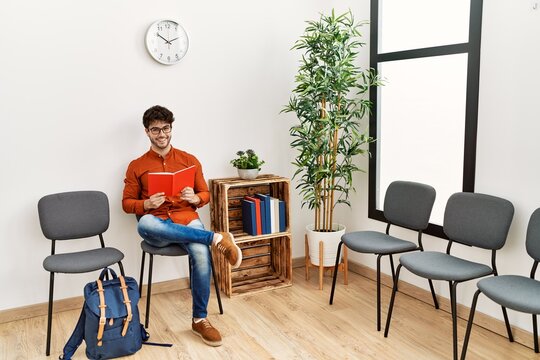 Young hispanic man smiling confident reading book at waiting room