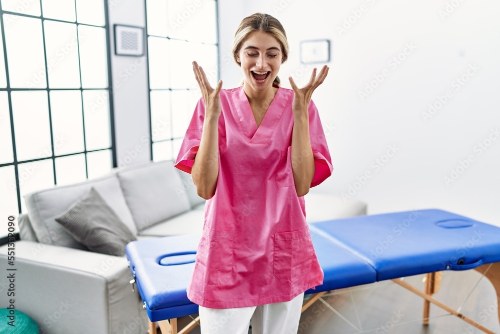 Canvas Prints Young blonde woman working as physiotherapist at home celebrating mad and crazy for success with arms raised and closed eyes screaming excited. winner concept