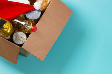 Christmas donation, charity, food bank, help for low income, poor families, migrants, refugees, homeless. Cardboard box full of grocery products and Christmas Santa hat. Top view