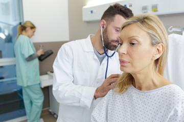 Obraz premium doctor listening through stethoscope to mature females back