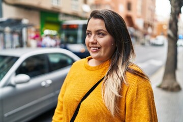 Fototapeta premium Young beautiful plus size woman smiling confident looking to the side at street